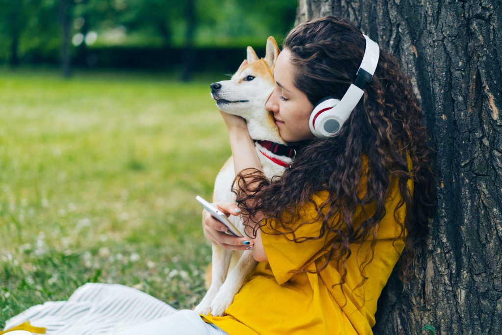 Woman hugging Shiba Inu dog while listening to music in a park.